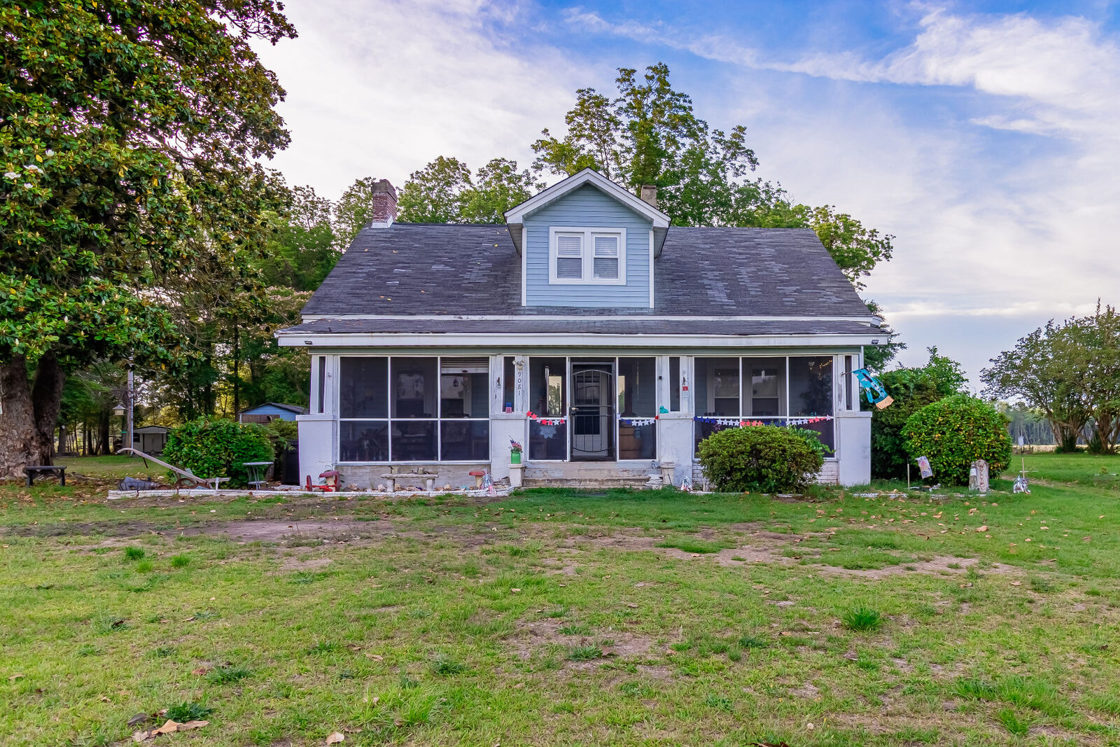Light blue farmhouse with a full screened front porch on a large grassy lot