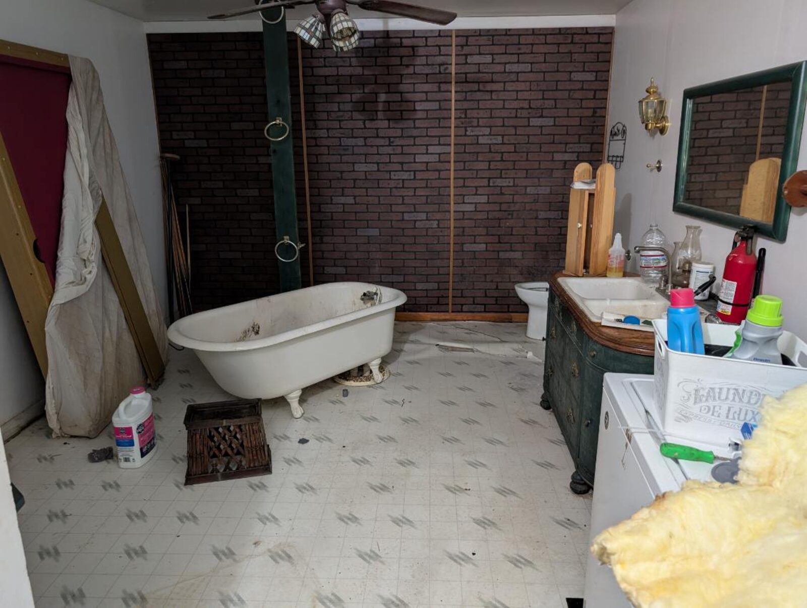 Dated bathroom with a stained clawfoot tub, faux brick wall and loose flooring