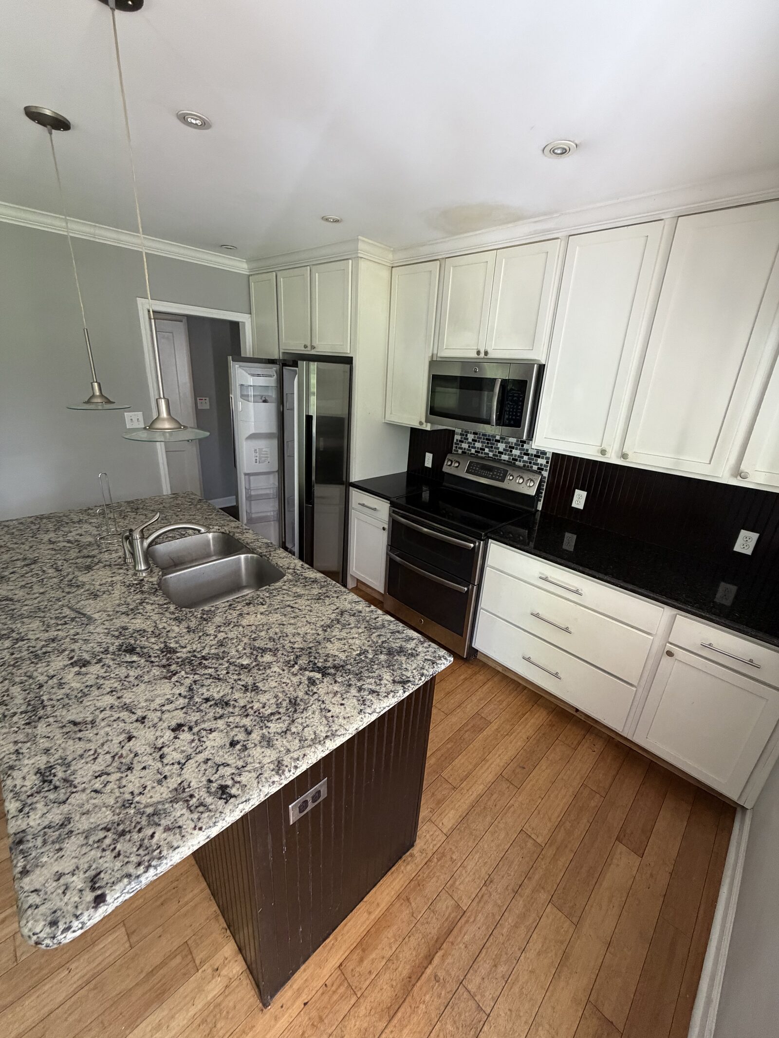 Kitchen with granite island, white cabinets and hardwood floors showing a ceiling water stain