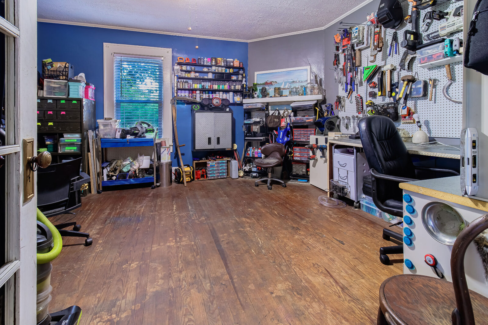 Workshop room packed with tools, pegboard walls and storage bins over worn wood floors