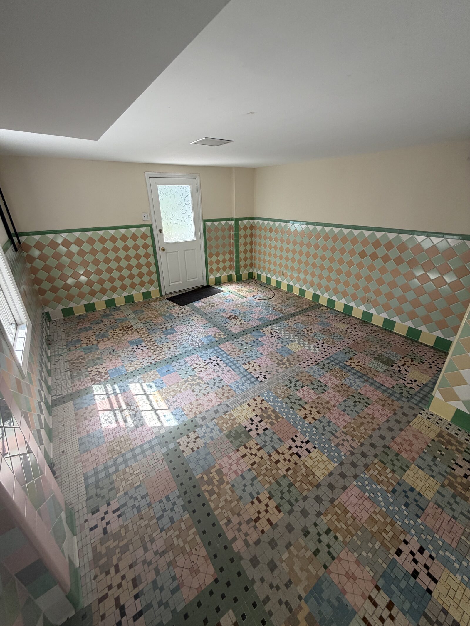 Empty room with vintage pastel mosaic tile floor and diamond-pattern tile wainscoting