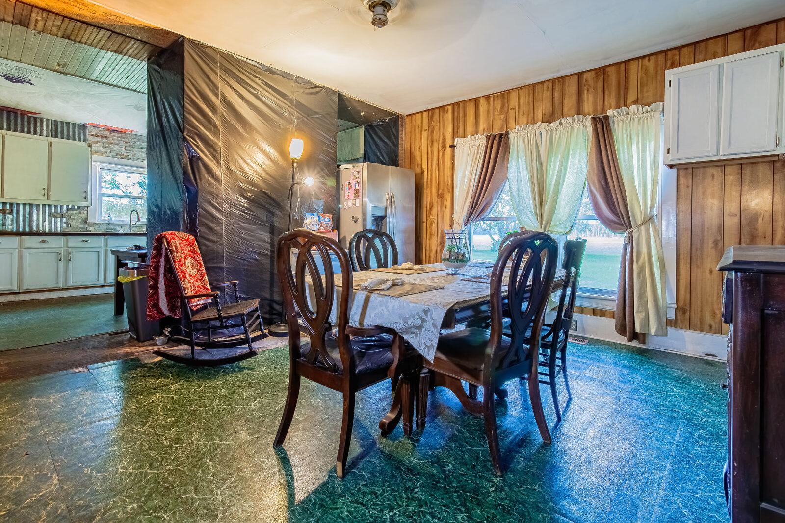 Dining room with wood paneling, green marbled floors and plastic sheeting over a doorway