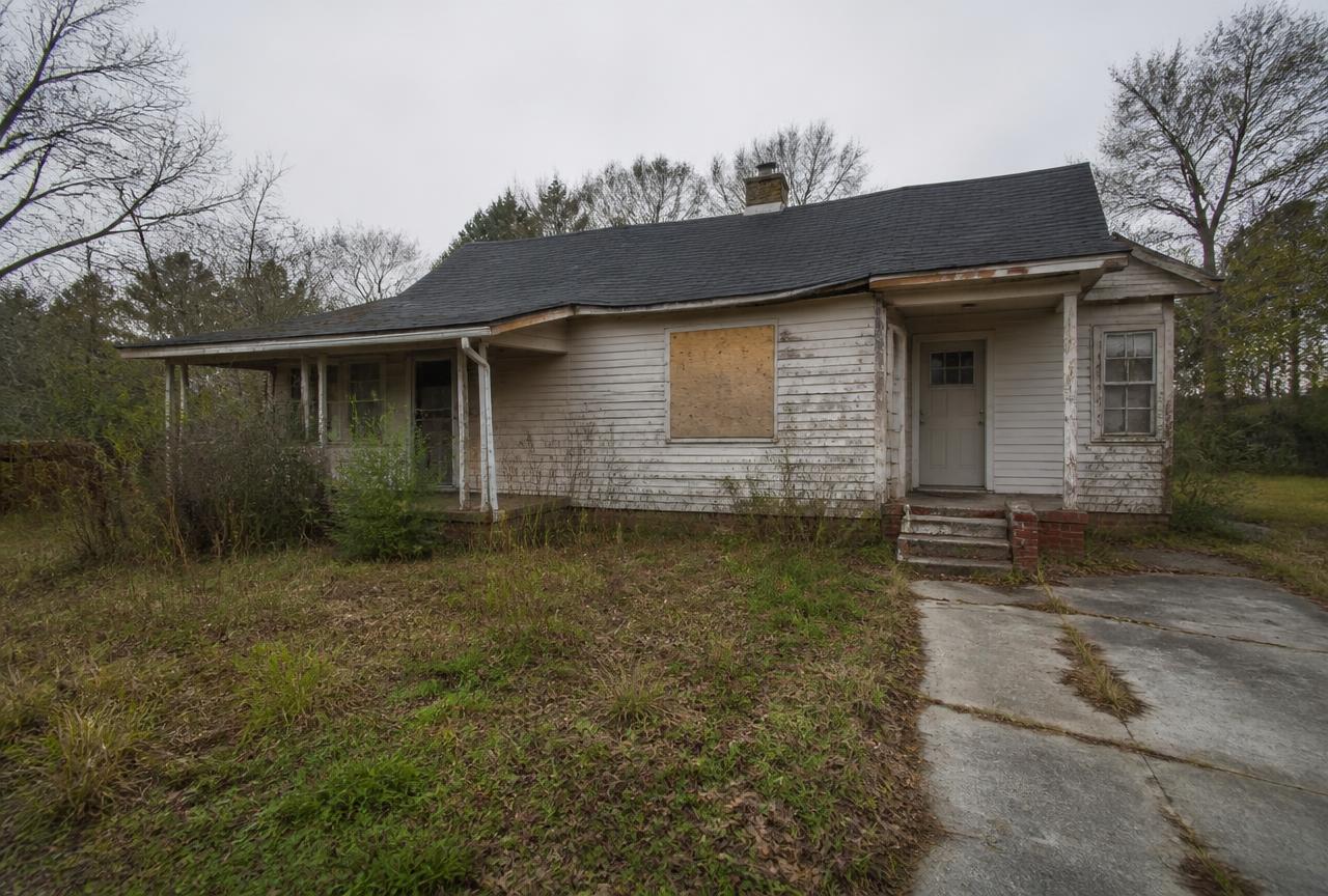 Vacant distressed house with peeling paint, boarded window and overgrown yard