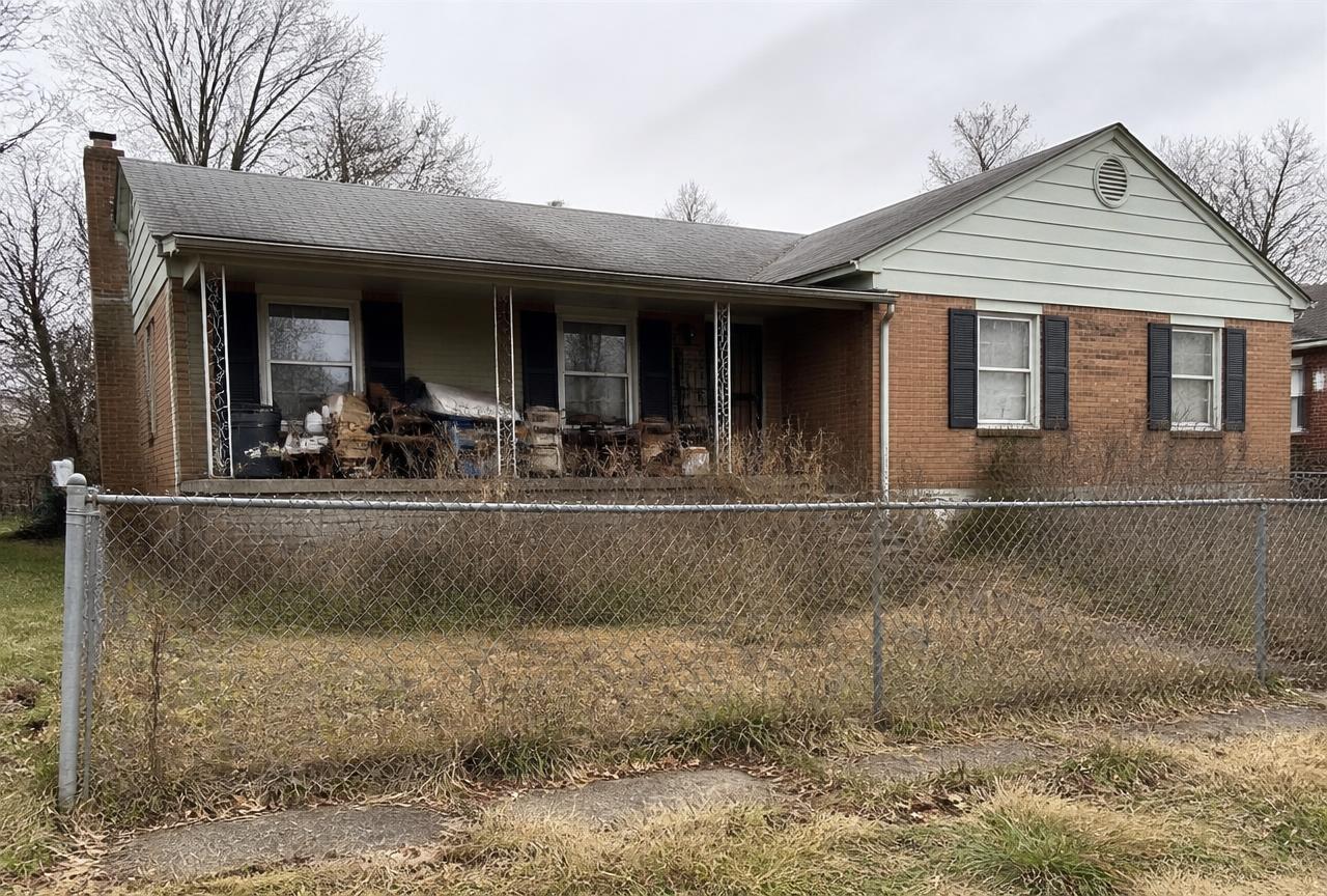 Neglected brick ranch house with junk piled on the porch and dead grass
